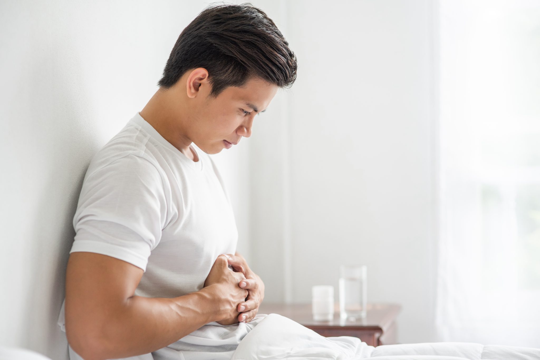 man-sits-bed-with-stomachache-presses-his-stomach-with-his-hands - Pharm-Dx Malaysia